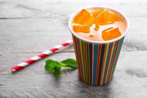 orange drink in bright paper cup on wooden background